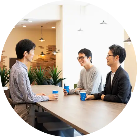 カフェスペースで飲み物を手にリラックスして談笑する3人の男性社員