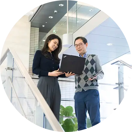 オフィスの吹き抜けでノートPCを見ながら相談する先輩社員と後輩社員