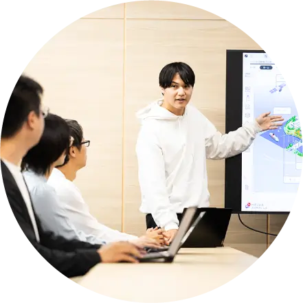 大型モニターで地図データを示しながらプレゼンする若手社員