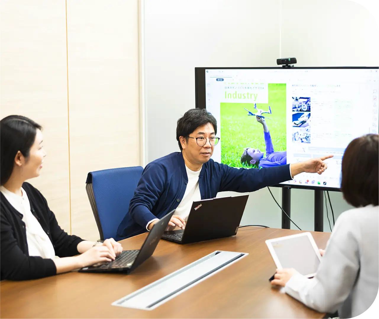 大型モニターで資料を示しながらチームメンバーと打ち合わせをするT.H