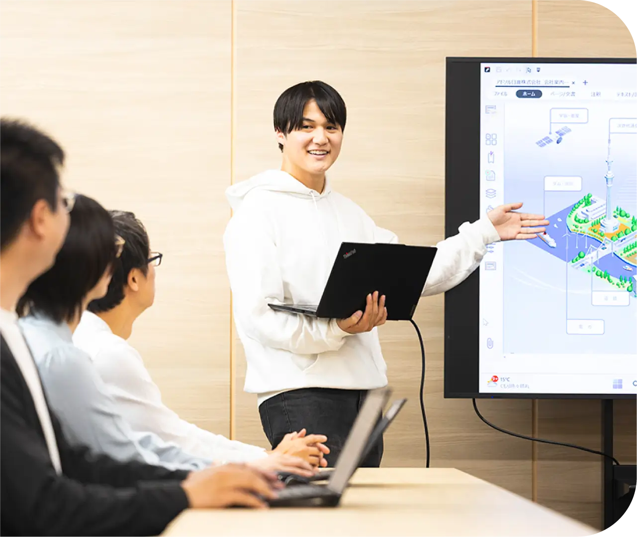 大型モニターでシステム構成図を示しながらチームにプレゼンするK.Y
