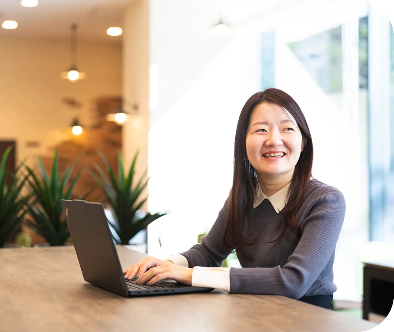 カフェスペースでノートPCを開き笑顔で作業するH.K