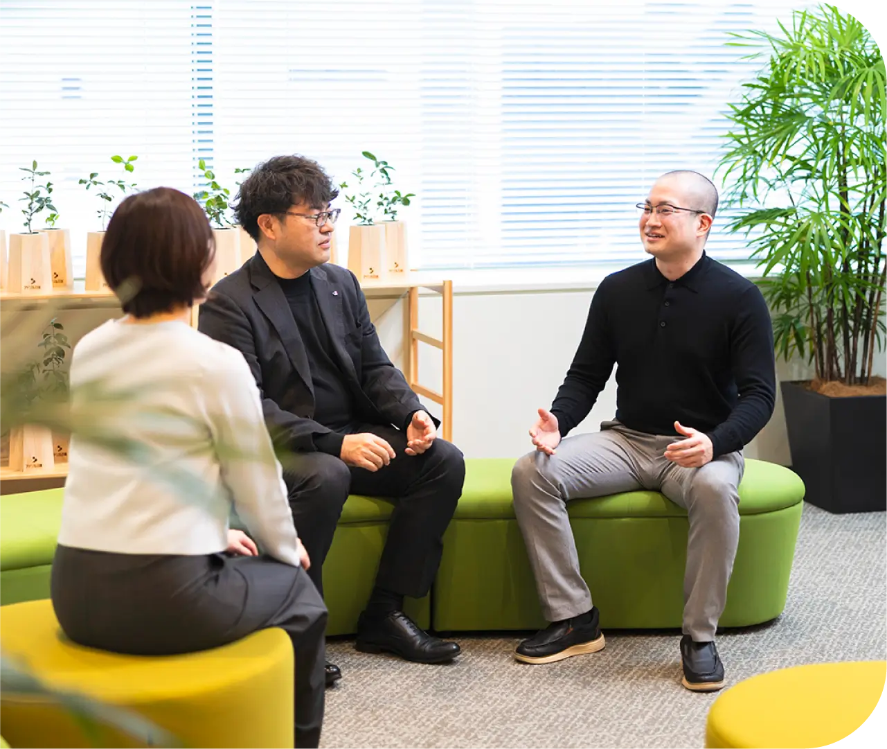 ラウンジのソファで同僚3人と笑顔で会話するT.Y