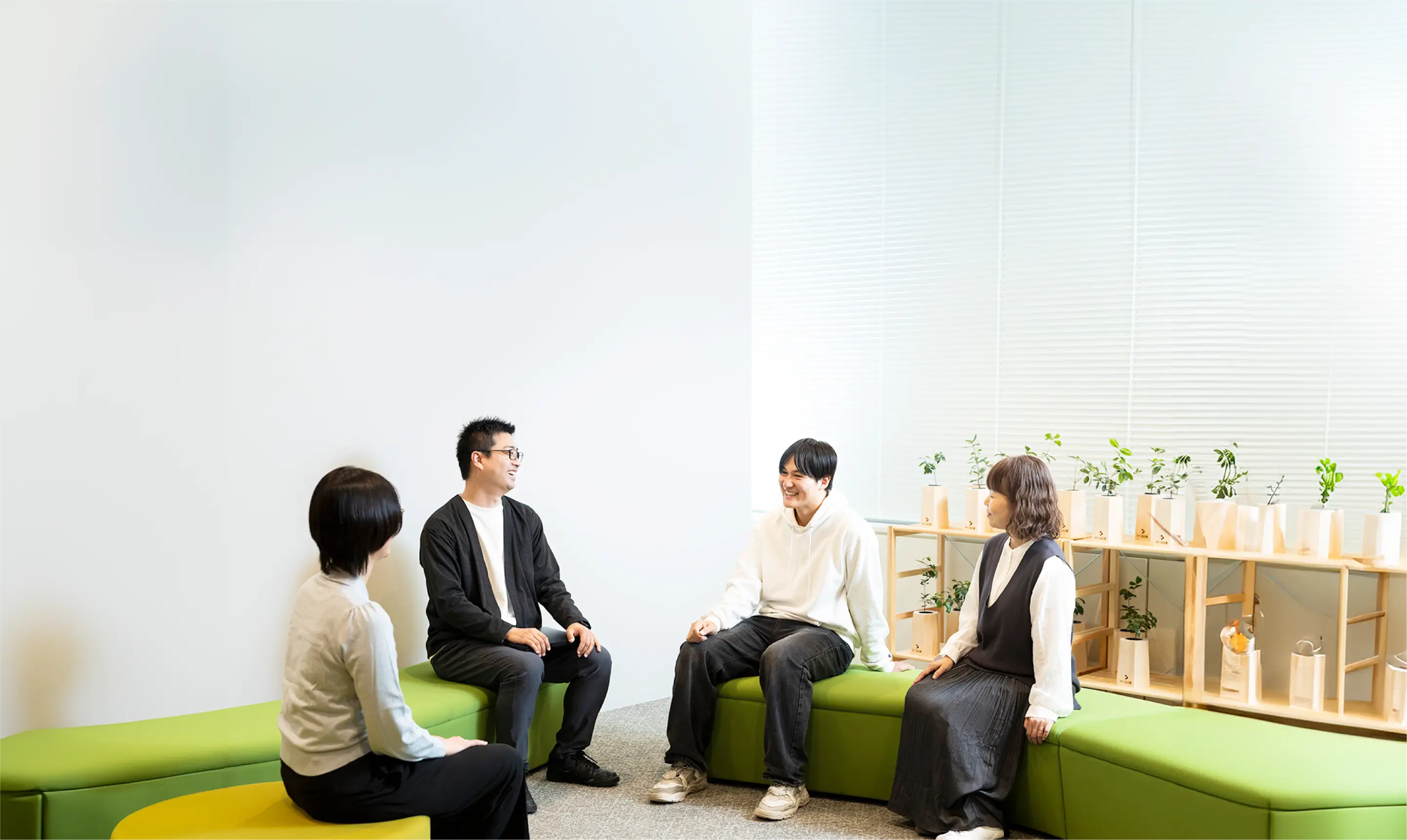 オフィスのラウンジで緑のソファに座り談笑する4人の社員